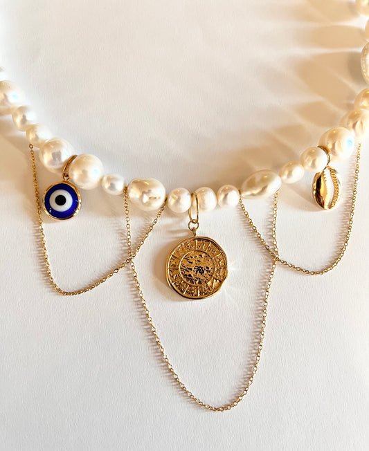 A completed pearl charm necklace with various charms including a coin and a blue bead, displayed on a light surface.