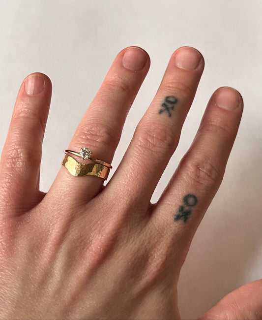 Eve Ring worn stacked on ring finger with a wide hammered gold band — 14k rose gold with diamond solitaire, on tattooed hand