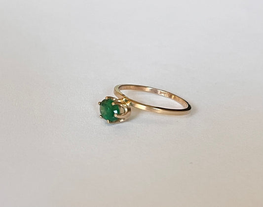 14k yellow gold emerald solitaire ring laying flat alongside plain gold band, showing stone setting detail, on white background