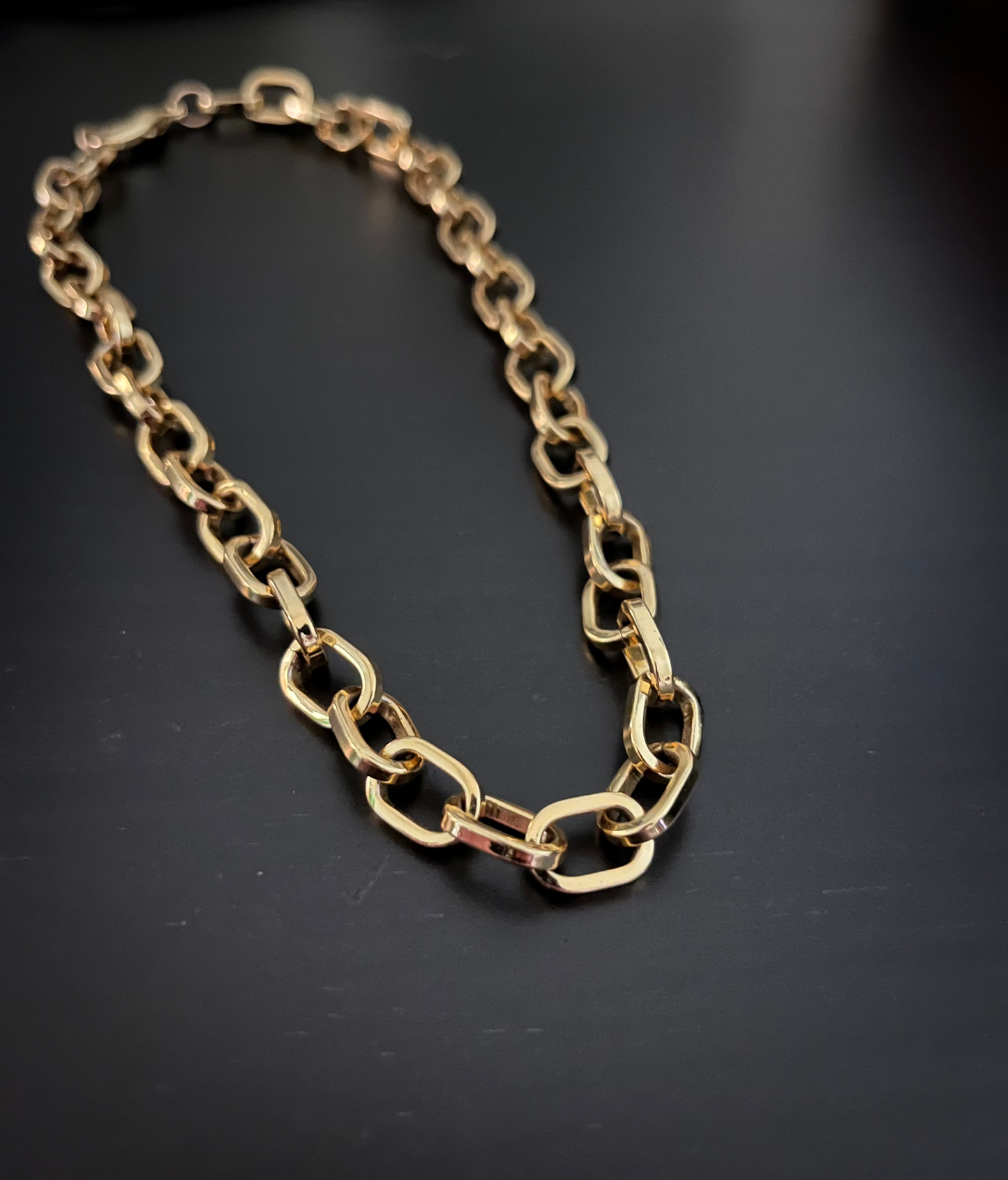 14k gold chunky oval link chain necklace with graduated links, high polish finish, laid flat on dark surface