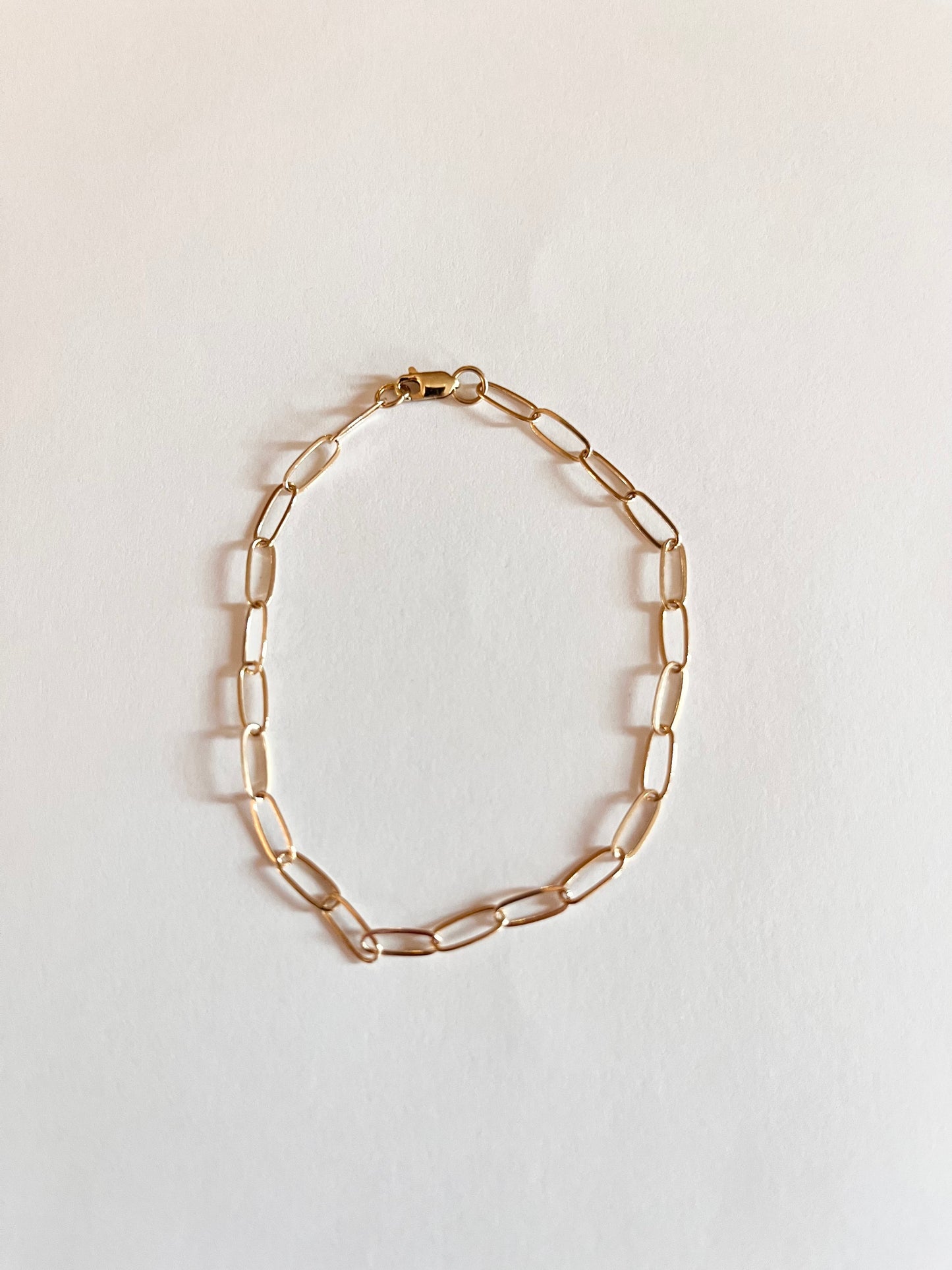 A gold mini paper clip chain bracelet on a white background.