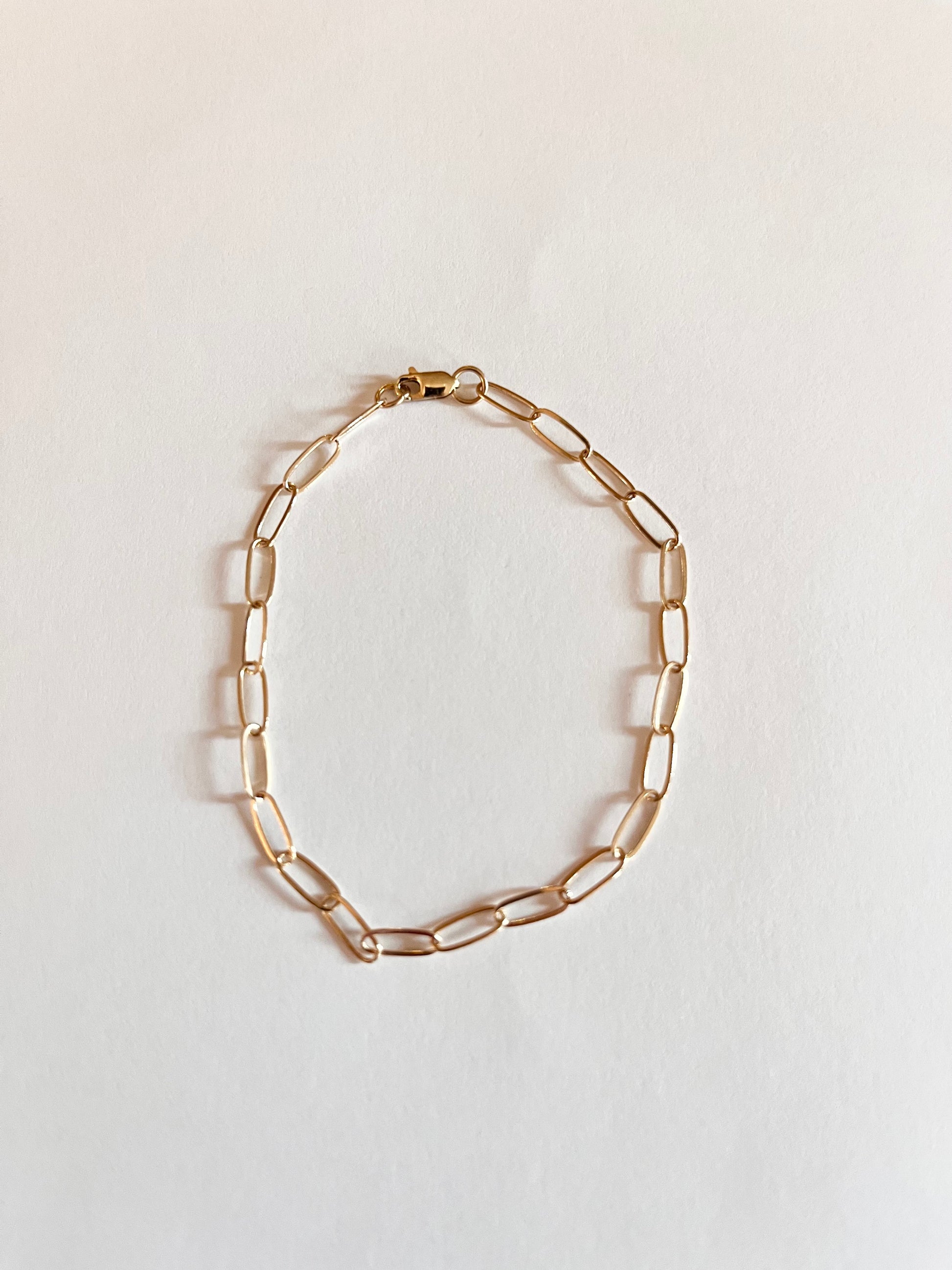 A gold mini paper clip chain bracelet on a white background.