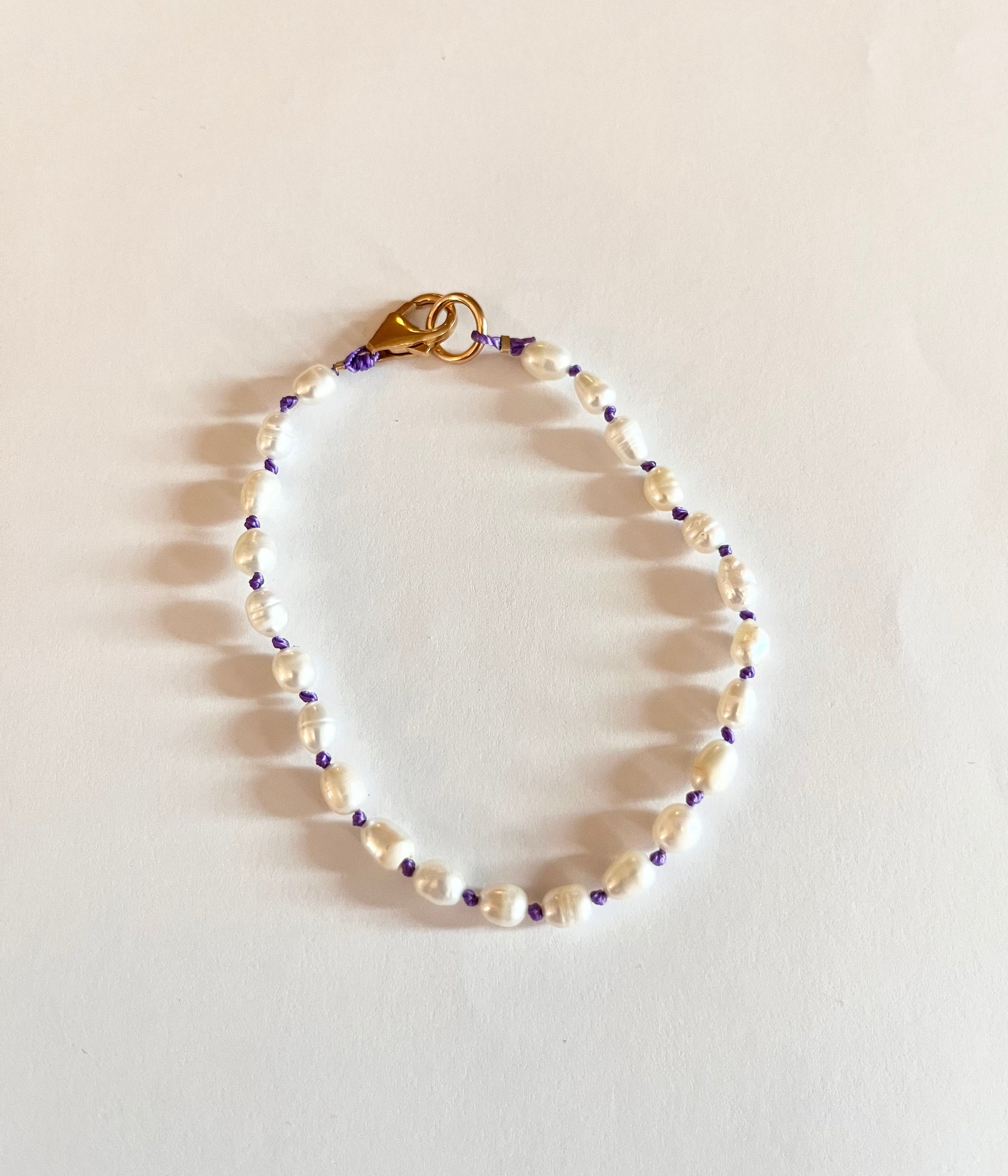 A handstrung bracelet with natural freshwater pearls and 14k gold findings, featuring lavender silk thread.